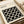 Minimalist Bauhaus-inspired poster with geometric pattern of white circles on black background, displayed in cream-colored frame on neutral textured surface alongside rolled paper tubes. Clean modernist design featuring repeated circular motifs in monochromatic color scheme, photographed at an angle showing the artwork's crisp geometric forms and gallery-style presentation.