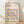 May include: A framed poster featuring colorful geometric circles in a grid pattern with "BAUHAUS" text at the top, displayed in a light wooden frame against a white wall on wooden flooring with natural window light casting shadows across the scene.