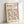 May include: Framed Bauhaus poster with colorful geometric circles in various bright colors including yellow, pink, blue, orange, and purple arranged in a grid pattern. The cream-colored print features "BAUHAUS" text at top with "Modernism, minimalism & abstract arts 1919-1933" and "School of Architecture Weimar, Dessau, Berlin" below. Light wood frame leans against white wall creating soft shadows.