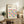 May include: Framed Bauhaus poster with colorful geometric circles in bright blues, yellows, pinks, and oranges displayed on rustic wooden sideboard alongside fern plant, ceramic vase, and stacked books in neutral living room setting with beige walls and upholstered furniture.