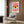 May include: Colorful Bauhaus-style poster with large eye design featuring red radiating lines, blue background, yellow and orange iris with dark blue pupil. Framed artwork displayed on wood-paneled wall above beige upholstered chair with geometric patterned pillow. Modern floor lamp with gold finish and open book on dark side table visible in minimalist interior setting.