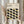 May include: Person in cream sweater holding framed poster with geometric pattern of interlocking oval shapes in black, olive green, and muted yellow on beige background. Dried pampas grass visible beside figure against soft neutral curtained backdrop.