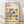 May include: Framed Bauhaus poster with colorful geometric shapes including circles, squares, triangles and rectangles in blue, red, orange, green and pink against cream background. Features "BAUHAUS" text and "School of Architecture Weimar, Dessau, Berlin" subtitle. Light wood frame sits on wooden floor against white wall with natural lighting creating soft shadows.