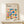 May include: Framed Bauhaus poster with colorful geometric shapes in red, blue, yellow, green, and pink arranged in grid pattern on cream background. Modern minimalist print displayed on light wood shelf with small wrapped gift box. Clean contemporary interior styling with neutral tones and natural lighting.
