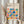 May include: Hands holding a framed Bauhaus-inspired poster with geometric shapes in blue, orange, green, pink, and red arranged in a grid pattern. The print features circles, squares, triangles, and semicircles on cream background with black text reading "BAUHAUS" and "School of Architecture Weimar, Dessau, Berlin" and dates "1919-1933". Light wood frame, neutral beige setting with dried pampas grass visible on left side.