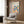 May include: Framed Bauhaus poster with colorful geometric shapes in red, blue, green, orange, and pink displayed on wood paneled wall above beige upholstered armchair with geometric patterned pillow. Modern brass floor lamp and dark round side table with open book complete the minimalist living room scene with light wood flooring.