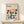May include: Framed Bauhaus poster with geometric pattern of colorful quarter-circle shapes in yellow, pink, blue, orange, and teal, displayed on light wood surface next to small wrapped gift with evergreen sprig against cream wall