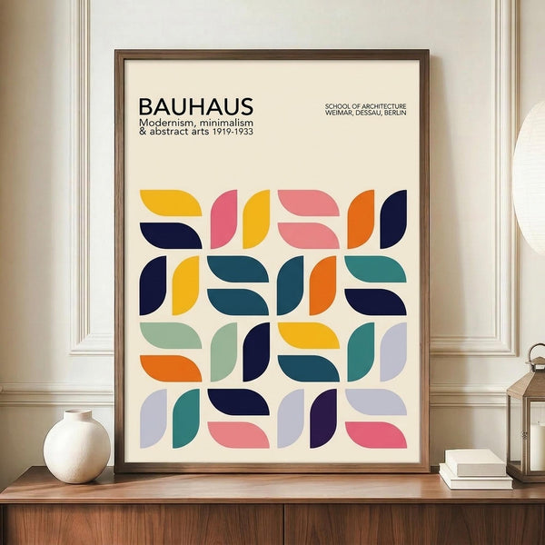 May include: Framed Bauhaus poster with colorful geometric semicircle pattern in navy, teal, orange, pink, yellow and purple on cream background, displayed on wooden sideboard next to white ceramic vase and books in elegant room with white wainscoting walls.