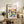 May include: Framed Bauhaus poster with colorful geometric semicircle pattern in yellow, pink, orange, navy, teal and green, displayed on rustic wooden sideboard next to fern plant, books, and ceramic vases in neutral living room setting with beige chair visible in corner.