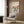 May include: Framed Bauhaus poster with colorful geometric leaf-like shapes in yellow, pink, orange, teal, and navy blue displayed on wood-paneled wall above light gray upholstered armchair with patterned pillow, next to brass floor lamp and dark round side table with open book