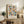 May include: Framed poster with colorful geometric circles and semicircles in muted pink, blue, green, orange and navy tones on cream background, displayed on rustic wood sideboard alongside fern plant, ceramic vase, and stacked books in cozy living room setting with beige upholstered furniture and soft natural lighting.