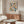 May include: Modern living room interior with geometric poster on wall featuring colorful circles and semicircles in pink, blue, green, orange, and black on cream background. Walnut credenza below with white mushroom lamp and copper floor lamp. White curved chair and glass-top oval coffee table complete the mid-century modern setting with neutral walls.