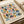 Modernist geometric poster featuring colorful circles divided into half and quarter sections in muted tones of sage green, dusty pink, navy blue, mustard yellow, and light blue on cream background. Text reads "BAUHAUS 1919-1933 SCHOOL OF ARTS & CRAFTS" in black lettering. Print lies flat on wooden surface next to rolled paper tubes, showing natural paper texture and clean graphic design style.