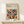 May include: Framed Bauhaus poster with geometric pattern of colorful overlapping semicircles in orange, teal, red, brown, and muted tones, displayed on light wood console table next to small wrapped gift with evergreen sprig, against cream wall with natural lighting