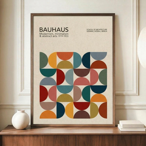 May include: Framed poster with geometric pattern of colorful semicircles and quarter-circles in squares, featuring text about Bauhaus modernism and minimalism. Earth-tone and jewel-tone colors including orange, teal, red, olive, and burgundy on cream background. Brown wooden frame displayed on walnut credenza next to white ceramic vase and stacked books in bright room with white paneled walls.