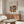 May include: Framed Bauhaus poster with colorful geometric circles and semicircles in red, blue, green, orange, and yellow arranged in a grid pattern, displayed above a mid-century walnut credenza with sliding doors. White modern chair and glass-top oval coffee table visible in minimalist living room setting with white walls and natural lighting.