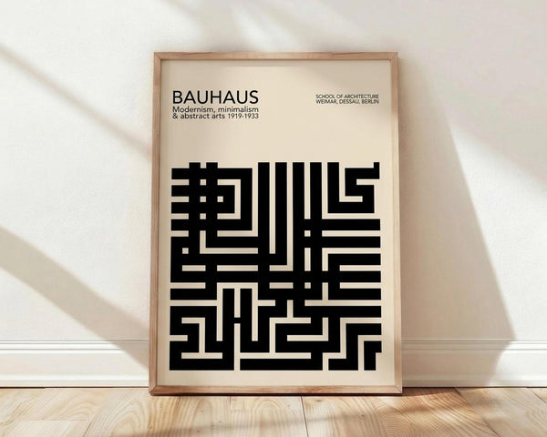 May include: Framed Bauhaus poster with geometric black typography on cream background, displayed in light wood frame against white wall on wooden floor. Minimalist modernist design featuring bold rectangular letterforms and text about the architecture school. Natural lighting creates soft shadows across the scene.