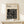 May include: Framed Bauhaus poster with black geometric maze-like pattern on cream background, displayed on light wood console table against beige wall. Small white gift box with greenery and gold bell sits in front of frame. Natural wood frame matches minimalist Scandinavian-style furniture. Soft natural lighting creates gentle shadows on textured wall surface.