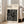 May include: Black and cream geometric abstract poster in light wood frame leaning against white wall next to beige upholstered chair. Design features bold rectangular maze-like pattern with "BAUHAUS" text and "Modernism, minimalism & abstract arts 1919-1933" subtitle. Natural lighting creates soft shadows on hardwood floor in minimalist room setting.