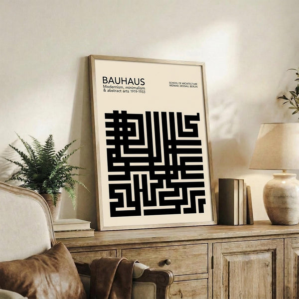 May include: Framed Bauhaus poster with black geometric maze-like pattern on cream background, displayed on rustic wooden sideboard alongside fern plant, stacked books, ceramic vase, and brown leather chair in warm-toned living room setting