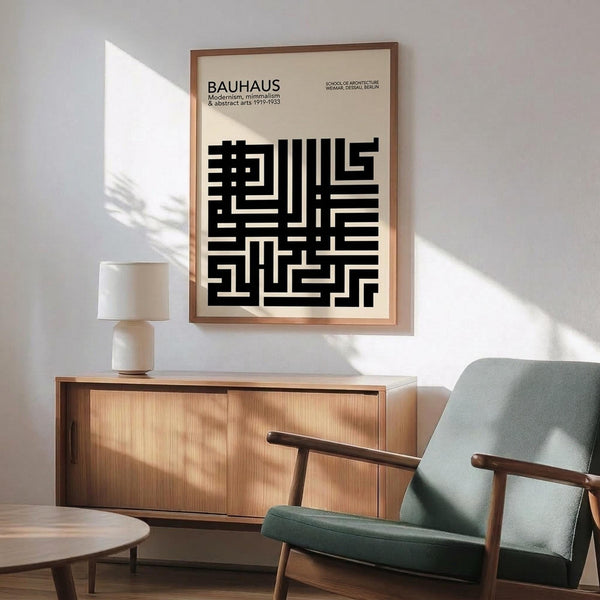 May include: Framed Bauhaus poster with black geometric maze-like pattern on cream background, displayed above wooden sideboard with table lamp in modern living room. Mid-century furniture includes sage green upholstered chair with wooden arms and round coffee table. Natural sunlight creates shadows on white wall.