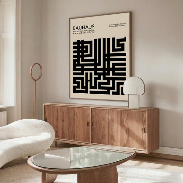 May include: Black and white geometric Bauhaus poster with abstract maze-like pattern mounted above wooden credenza in modern living room. Cream colored sculptural chair and glass coffee table visible. Minimalist interior with neutral tones and natural lighting from window.
