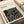 May include: Bauhaus poster print in cream color with bold black geometric maze-like pattern displayed flat on white surface beside rolled paper tubes. The minimalist design features angular interlocking shapes creating an abstract labyrinth effect, with text at top referencing the German design school from 1919-1933. Clean modernist aesthetic with high contrast black and white color scheme.