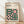 May include: Framed Bauhaus modernist poster with geometric design featuring green circles and pink squares arranged in abstract patterns. Cream background with black text reading "BAUHAUS Modernism, minimalism & abstract arts 1919-1933" and "SCHOOL OF ARCHITECTURE WEIMAR, DESSAU, BERLIN." Light wood frame displayed against white wall on wooden floor with natural lighting creating soft shadows.