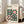 May include: Framed Bauhaus-inspired poster with geometric pattern in green and pink colors, featuring circles and squares in modernist style. Light wood frame leaning against white wall next to beige upholstered chair in bright living room with large windows and natural lighting on wooden floors.