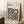 May include: A framed Bauhaus poster with geometric green circles and pink squares on cream background, leaning against white wall beside wooden cube table with white coffee cup and beige textured throw blanket on white fluffy rug.