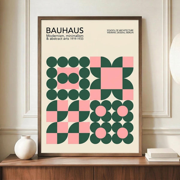 May include: Framed Bauhaus-style poster with geometric design featuring pink and dark green circles, quarter-circles, and squares arranged in a grid pattern. Text reads "BAUHAUS Modernism, minimalism & abstract arts 1919-1933" and "SCHOOL OF ARCHITECTURE WEIMAR, DESSAU, BERLIN." Brown wooden frame displayed on wooden sideboard alongside white ceramic vase and stacked books in elegant room with cream walls and white molding.