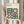 May include: Person holding framed Bauhaus-inspired geometric poster with pink and dark green circles, squares, and curved shapes arranged in grid pattern. Light wood frame against neutral background with dried pampas grass visible to left. Cream colored background with minimalist typography at top.