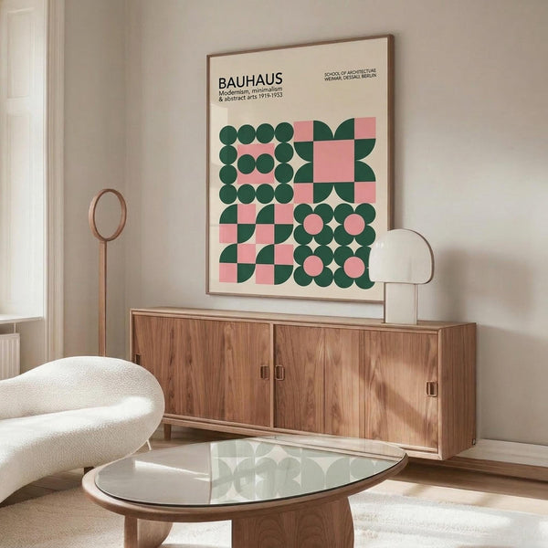 May include: Framed Bauhaus poster with geometric green and pink circles and squares displayed above a mid-century wooden credenza in a minimalist living room. White curved chair and glass coffee table visible in foreground. Warm wood tones and neutral wall colors create modern Scandinavian-inspired interior styling.