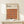May include: Framed Bauhaus poster with geometric pattern of overlapping circles in warm autumn colors - orange, burgundy, brown, and rust tones arranged in rows. The minimalist design features text about modernism and abstract arts from 1919-1933. Natural wood frame sits on light wooden surface against cream wall, with small wrapped gift box placed in front.