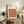 May include: Framed Bauhaus poster with geometric pattern of overlapping circles in warm autumn colors - oranges, browns, and burgundy - displayed on rustic wooden sideboard alongside fern plant, ceramic vases, and stacked books in neutral-toned living room setting