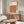 May include: Framed Bauhaus poster with geometric pattern of overlapping circles in warm orange, burgundy, and brown tones displayed above wooden sideboard in modern living room. White upholstered chair and glass-top coffee table visible. Minimalist interior with neutral walls and natural lighting creating soft shadows.