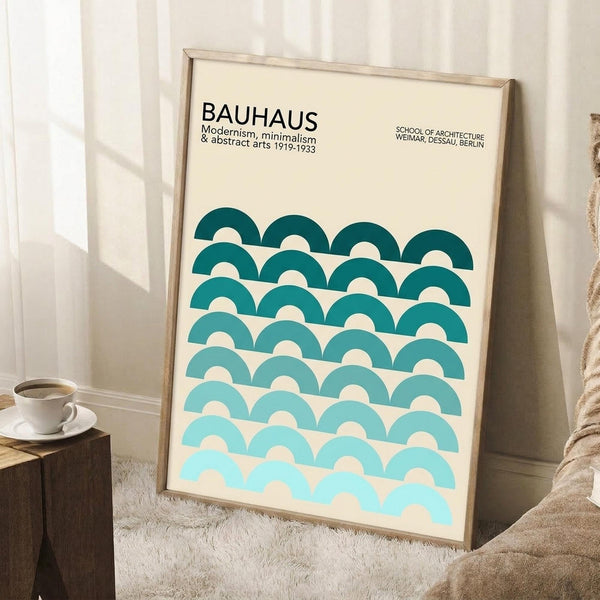 May include: Framed Bauhaus poster with cream background and geometric pattern of overlapping teal semicircles in gradient shades, leaning against white wall corner. Scene shows wooden side table with white coffee cup, beige knit throw, and white area rug. Minimalist modern home decor styling with natural lighting.