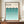 May include: Framed Bauhaus poster with gradient teal semicircle pattern displayed on wooden sideboard next to white ceramic vase and books. The minimalist print features rows of overlapping half-circles transitioning from dark teal at top to light aqua at bottom against cream background. Brown wooden frame sits in room with white wainscoting and warm lighting.