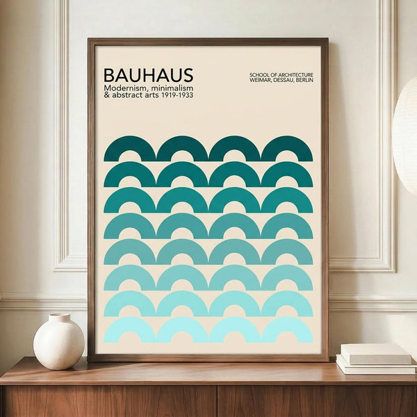 May include: Framed Bauhaus poster with gradient teal semicircle pattern displayed on wooden sideboard next to white ceramic vase and books. The minimalist print features rows of overlapping half-circles transitioning from dark teal at top to light aqua at bottom against cream background. Brown wooden frame sits in room with white wainscoting and warm lighting.