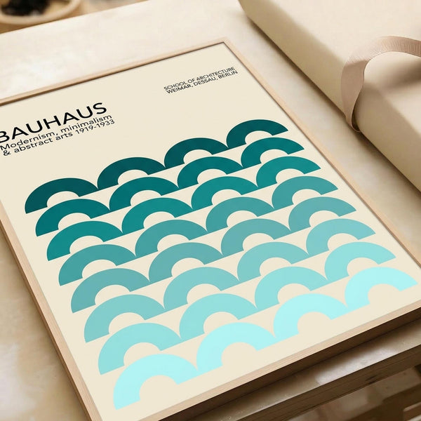 Minimalist Bauhaus poster with repeating wave pattern in gradient teal and turquoise semicircles on cream background. Text reads "BAUHAUS" and "School of Architecture Weimar, Dessau, Berlin" with "Modernism, minimalism & abstract arts 1919-1933". Print displayed on wooden surface next to rolled white paper tube, showing clean geometric design typical of Bauhaus movement.