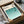 May include: Framed Bauhaus poster with teal and turquoise geometric wave pattern and minimalist black periscope design, displayed in black frame inside cardboard shipping box with protective tissue paper wrapping