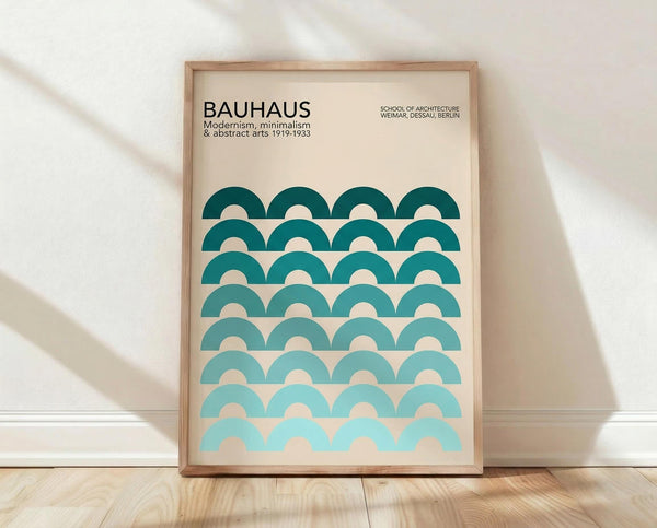 May include: Framed Bauhaus modernist poster with teal gradient semicircle pattern arranged in rows, displayed against white textured wall on light wood floor with natural sunlight shadows. Features cream background with typography referencing the influential German design school's 1919-1933 period in Weimar, Dessau, and Berlin.