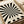 Black and white radial optical illusion design with alternating stripes radiating from center point, creating a hypnotic sunburst pattern with wavy, distorted edges. Text reads "BAUHAUS 1919-1933 SCHOOL OF ARTS & CRAFTS" in clean typography. Print shown in light wooden frame on neutral surface alongside rolled paper tubes.