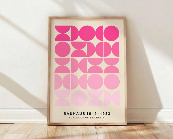 May include: A framed geometric art print featuring pink semicircles and circles arranged in a grid pattern, displayed in a light wood frame against a white wall on wooden flooring with soft natural lighting creating shadows across the scene.
