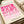 May include: Pink geometric abstract art print in wooden frame displayed on neutral fabric surface next to wrapped gift with ribbon and small green plant. The artwork features overlapping circles and curved shapes in gradient pink tones from bright fuchsia to pale pink on cream background, with black text reading "BAUHAUS 1919-1933 SCHOOL OF ARTS & CRAFTS" in lower corner.