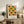May include: Framed geometric poster with alternating green and orange circles and semicircles arranged in a grid pattern, displayed on rustic wooden sideboard alongside fern plant, ceramic vase, and stacked books in neutral-toned living room setting.