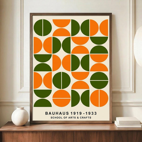 May include: Framed geometric poster with green and orange circles and semicircles arranged in a grid pattern on cream background, displayed on wooden sideboard next to white ceramic vase and stacked books in modern interior with white paneled walls.