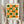May include: Person in beige ruffled sleeves holding framed geometric art print with orange and green circles and semicircles arranged in grid pattern. Light wooden frame against cream background. Dried pampas grass visible to left. Soft natural lighting near white curtained window.