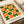 May include: Framed geometric art print featuring repeating pattern of split circles in orange and olive green on cream background. Print displays "BAUHAUS 1919-1933 SCHOOL OF ARTS & CRAFTS" text at bottom. Wooden frame sits on light wooden surface next to white sculptural objects, showing mid-century modern minimalist aesthetic with warm neutral tones.