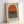 May include: Framed minimalist poster featuring large orange semicircle above horizontal black and white stripes on cream background, displayed in light wood frame leaning against white wall corner. Clean geometric design with "BAUHAUS 1919-1933 SCHOOL OF ARTS & CRAFTS" text at bottom in black sans-serif font.